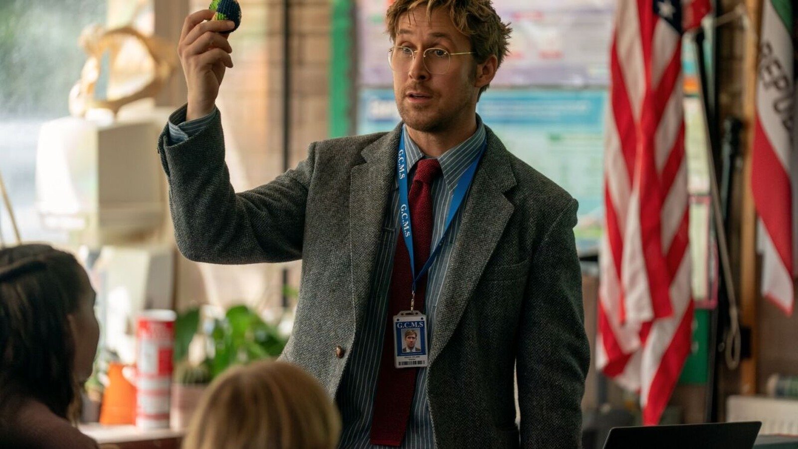 A scene from Project Hail Mary starring Ryan Gosling in a classroom demonstrating object, flag in background