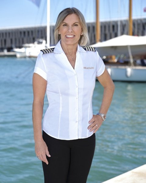 Captain Sandy Yawn smiling in her uniform in front of a marina.